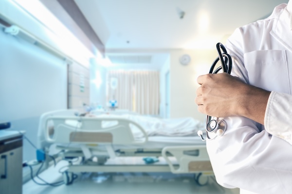 hand of doctor holding stethoscope with blurred background of recovery patient room with patient bed in hospital