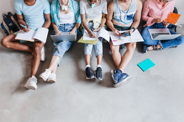 Overhead portrait of students in trendy sneakers chilling on the floor while preparing for exams together. University friends spending time together using laptops and writing abstract.